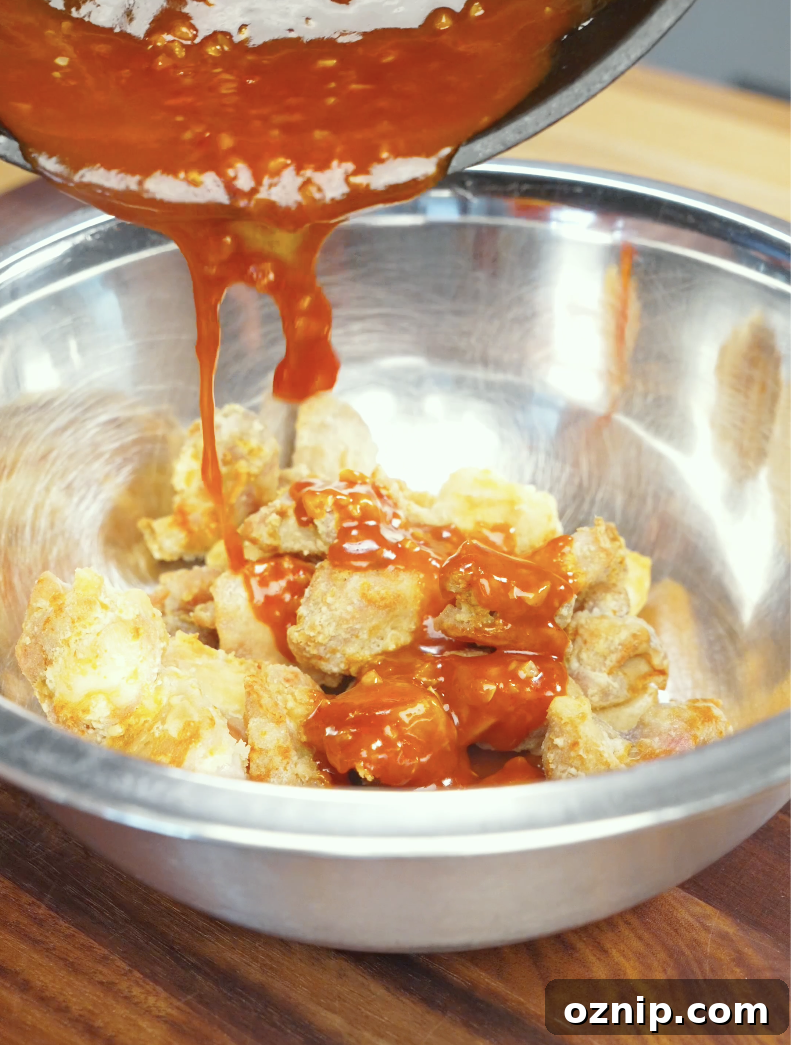 Thick homemade gochujang sauce being poured over crispy air-fried chicken pieces in a mixing bowl. The glossy Korean-inspired glaze coats every piece for maximum flavor.