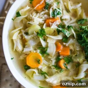 Chicken noodle soup in a white bowl with crackers around it