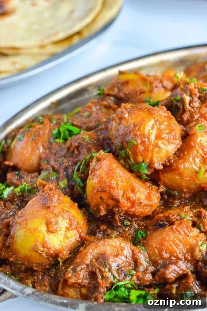 Restaurant Style Bombay Potatoes Recipe 2 angled view of potatoes in brown sauce with fresh herbs sprinkled on top and roti in the background