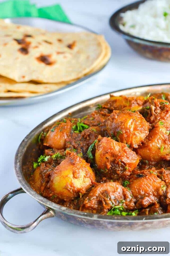Restaurant Style Bombay Potatoes Recipe 8 A silve pan of bombay potatoes with roti and rice in the background on a white surface