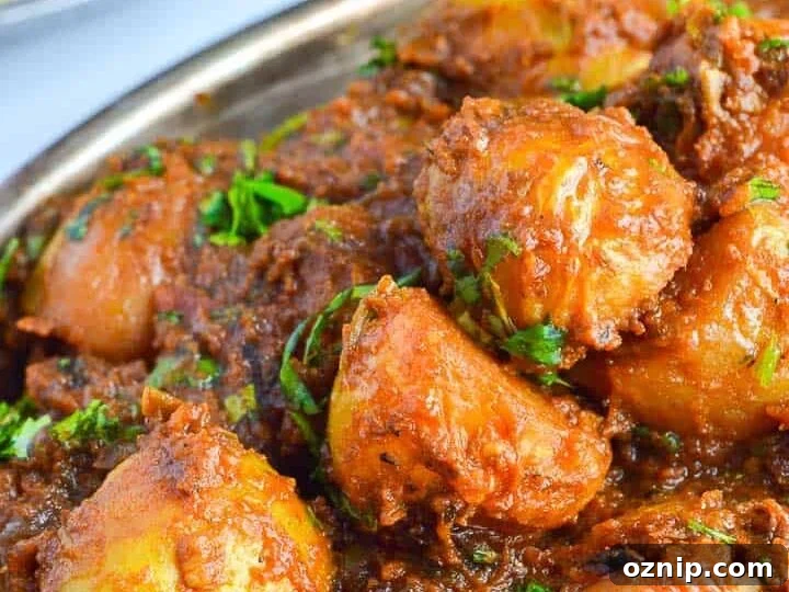 angled view of potatoes in brown sauce with fresh herbs sprinkled on top and roti in the background