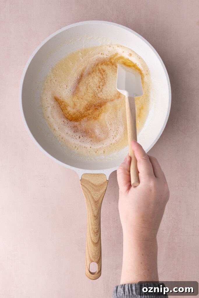 Buttery Crunch Cookies: Chewy Centers, Crispy Edges 4 Butter browning in a white pan being stirred with a rubber spatula.