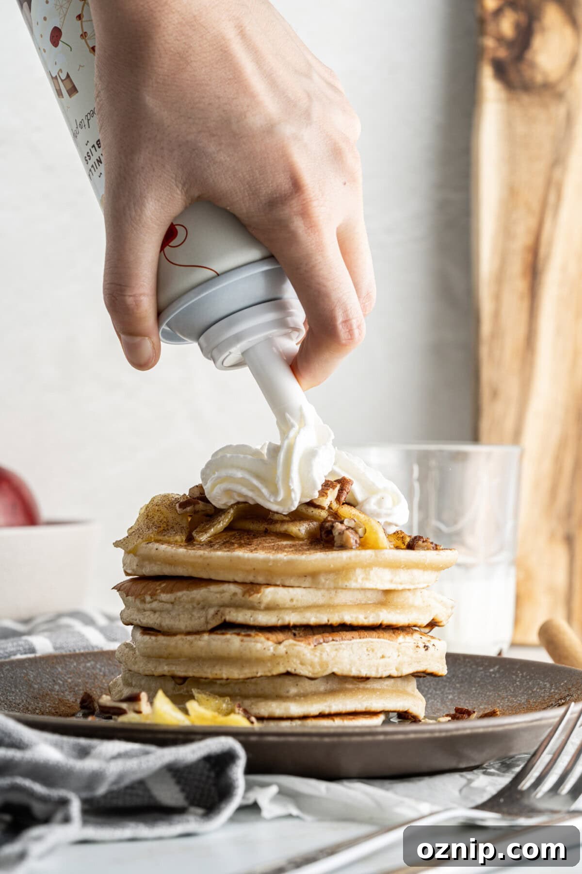 adding whipped cream to a stack of Apple Pancakes