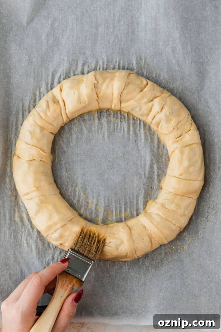 Flaky Bacon and Brie Crescent Wreath Recipe 11 A hand using a pastry brush to brush a bacon and brie crescent wreath with egg wash.
