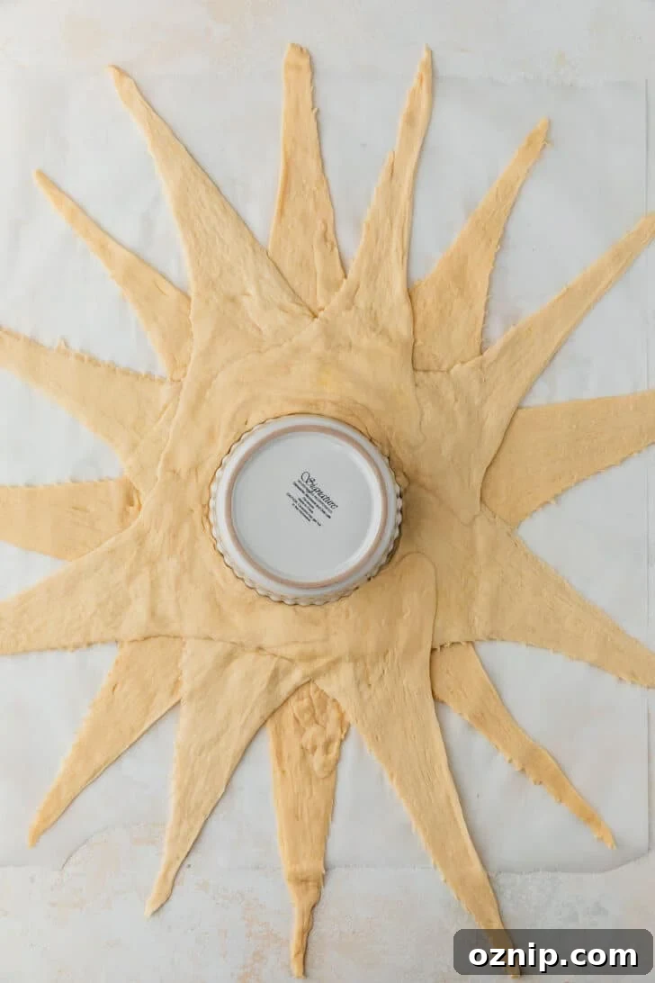 Flaky Bacon and Brie Crescent Wreath Recipe 4 Croissant dough in a sunburst shape on a white counter.