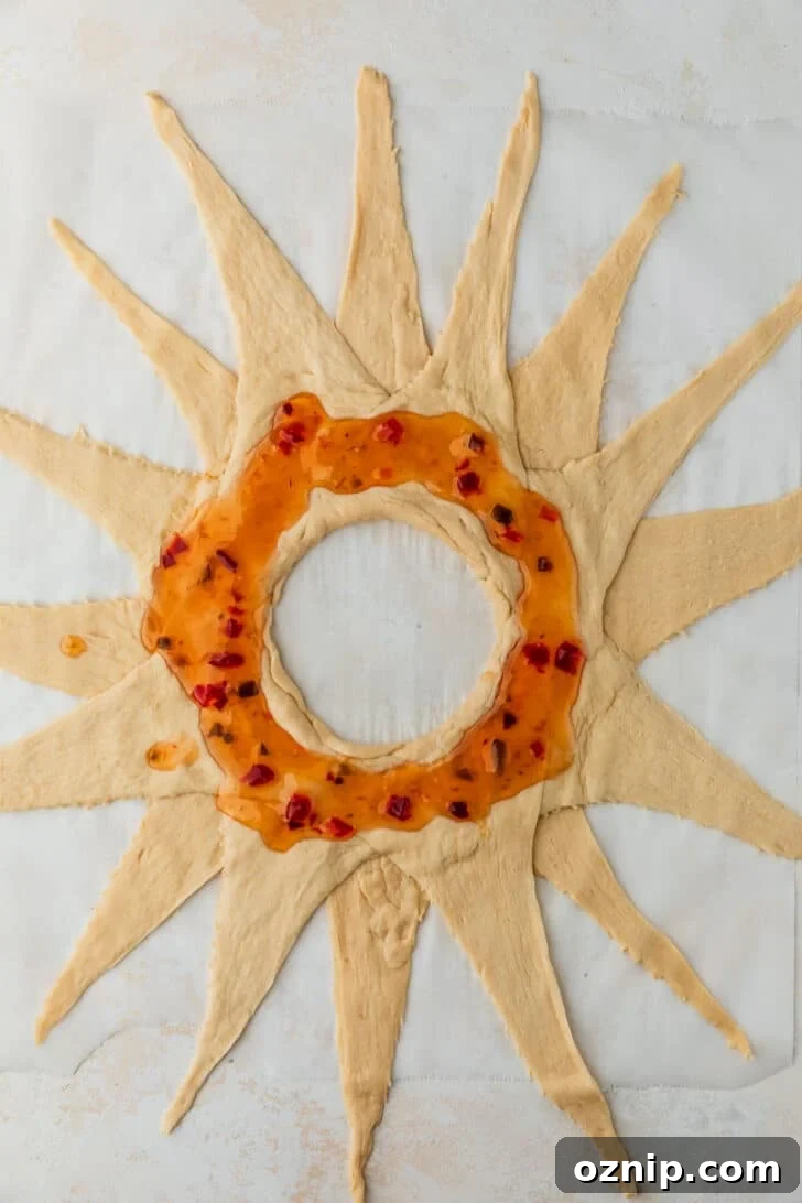 Flaky Bacon and Brie Crescent Wreath Recipe 5 Croissant dough in a starburst shape with pepper jelly on parchment paper.