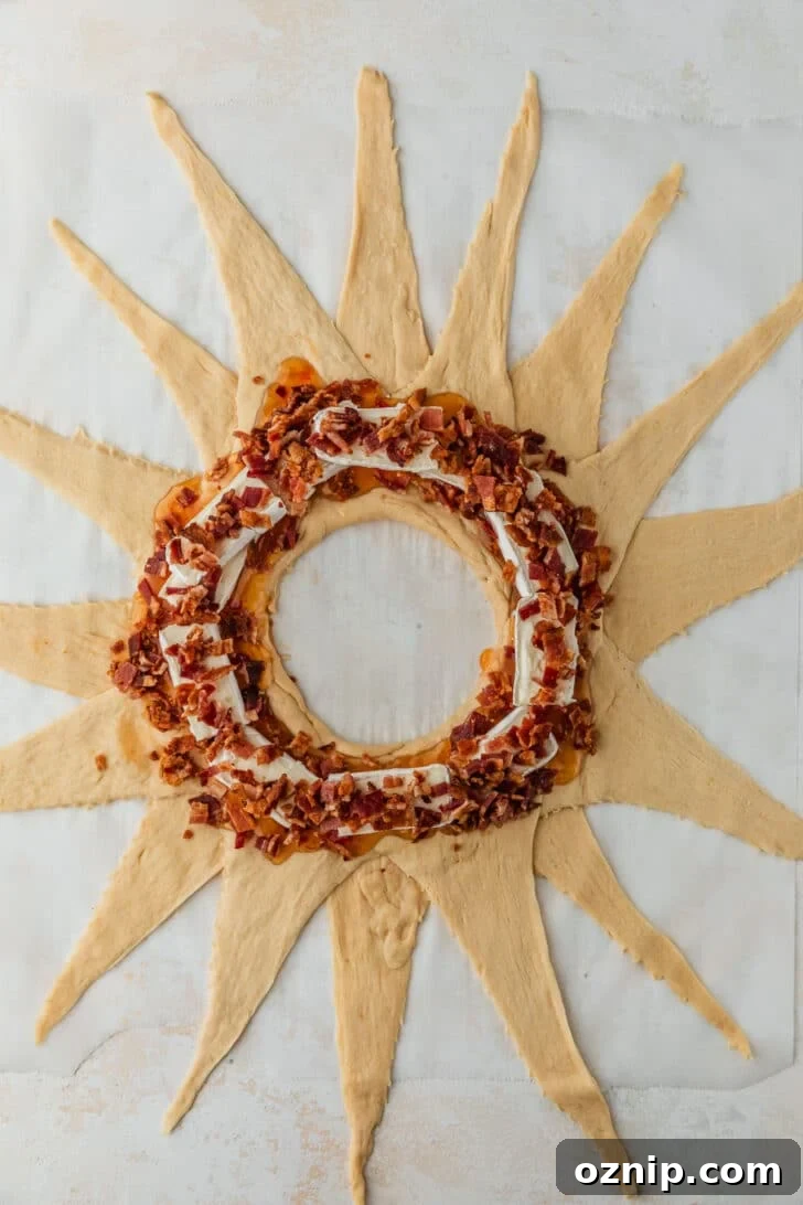 Flaky Bacon and Brie Crescent Wreath Recipe 6 Crescent dough in a star shape with brie and bacon on a white counter.