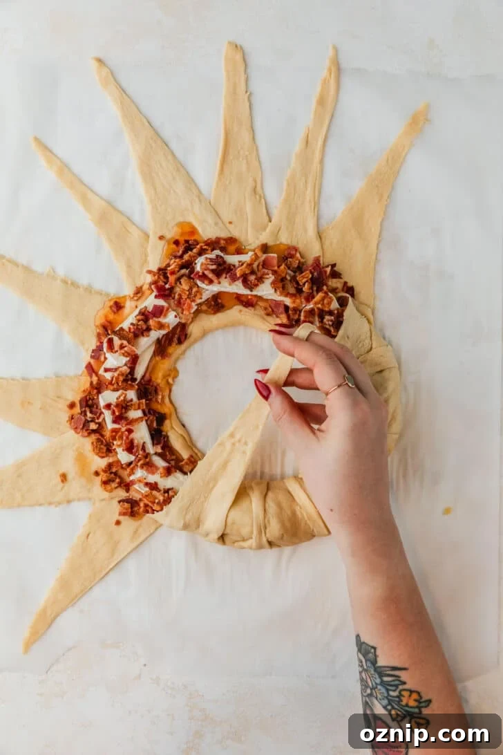 Flaky Bacon and Brie Crescent Wreath Recipe 7 A hand shaping a bread wreath on white parchment paper.