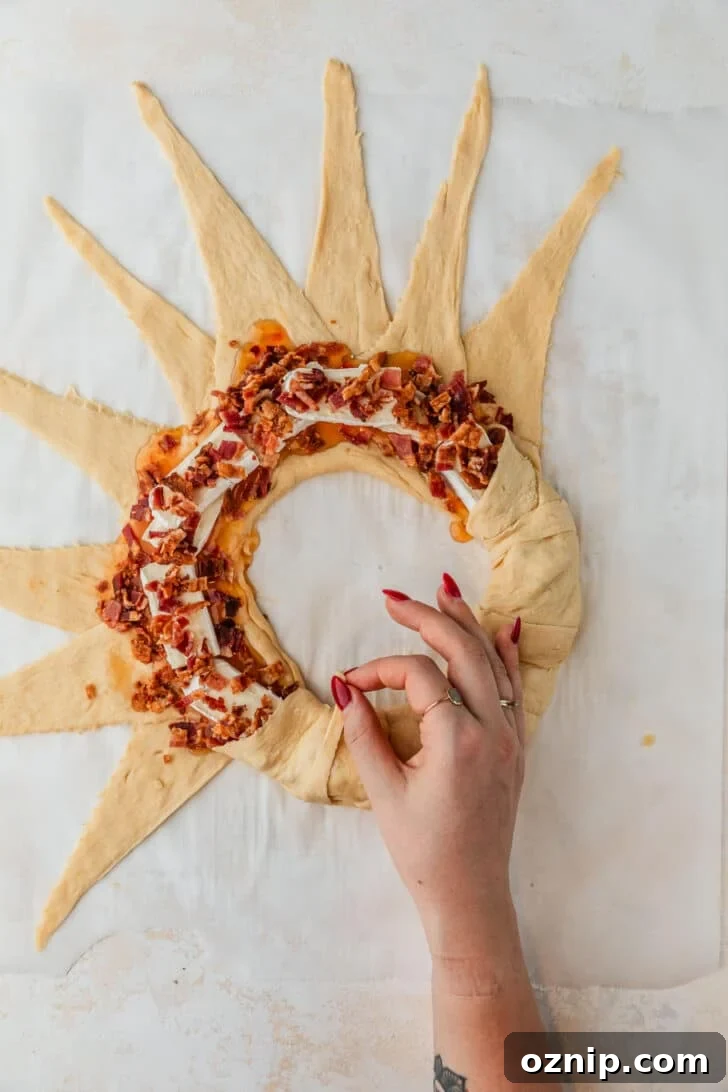Flaky Bacon and Brie Crescent Wreath Recipe 9 Hands forming a bacon and brie crescent wreath on parchment paper.
