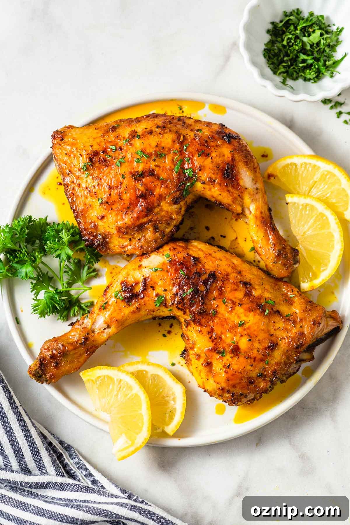 air fryer chicken leg quarters on a plate with parsley and lemon wedges on the side.