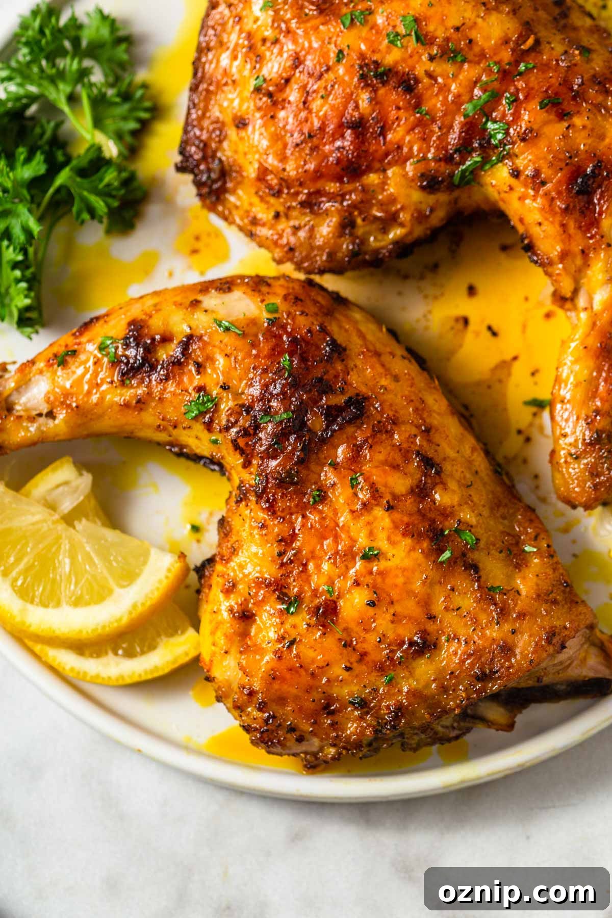Two crispy and golden chicken leg quarters on a plate with parsley and lemon wedges.