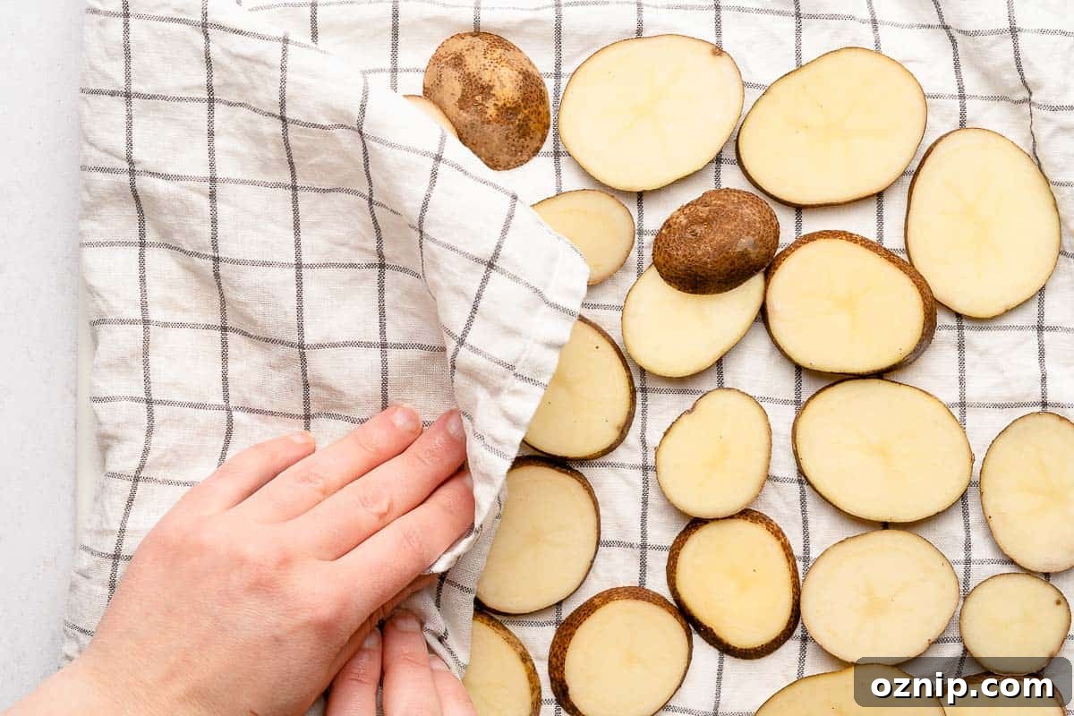 hand blotting sliced potatoes with kitchen towel