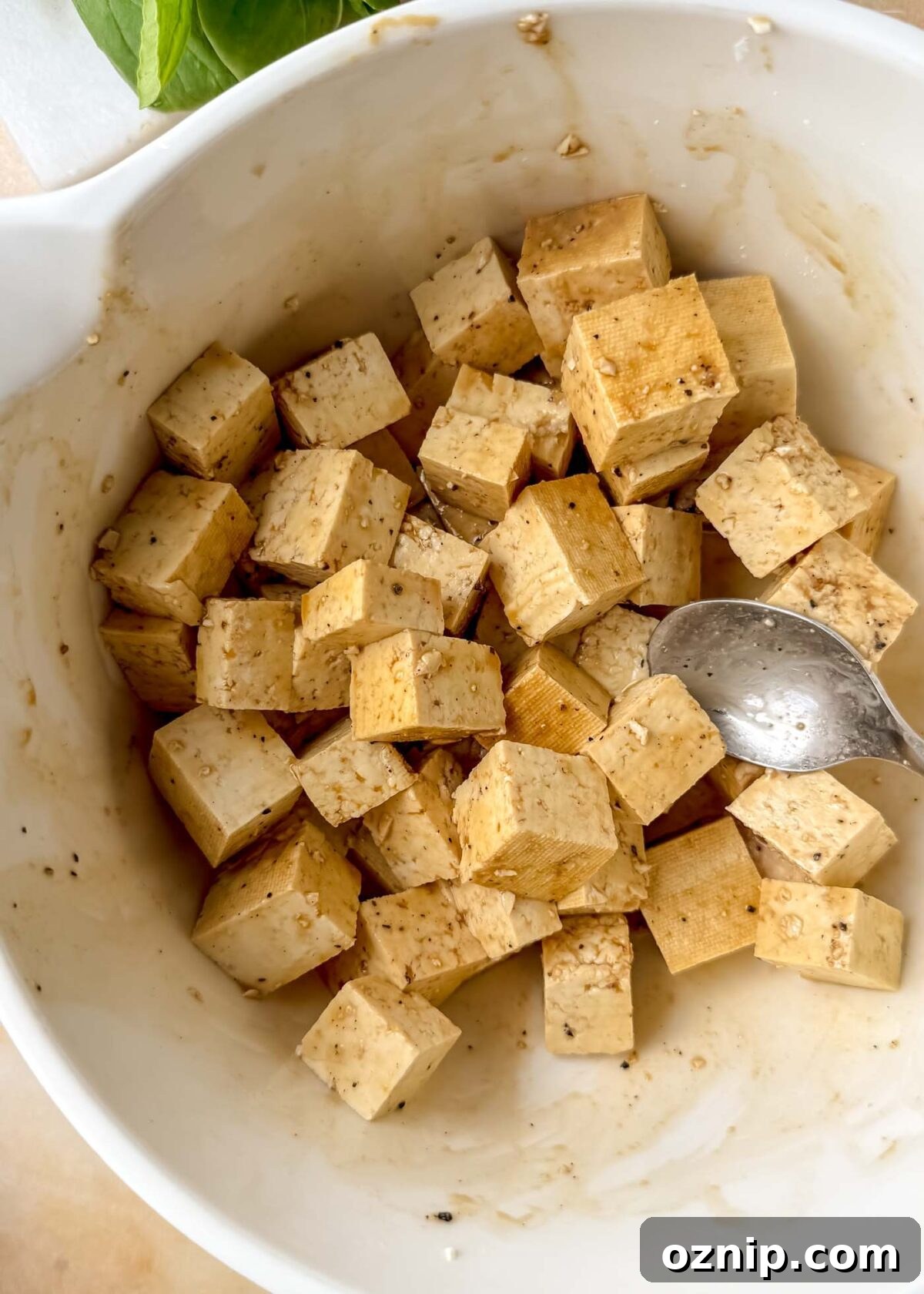 Sesame-Ginger Tofu Soba Noodles 4 Cubed tofu coated in a light brown marinade inside a white mixing bowl before cooking.