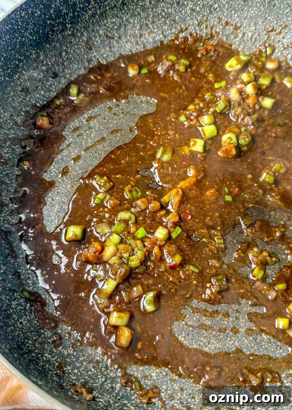 Sesame-Ginger Tofu Soba Noodles 8 Dark glossy sesame-soy sauce simmering in a pan with chopped green onions, garlic, and small chili flakes.