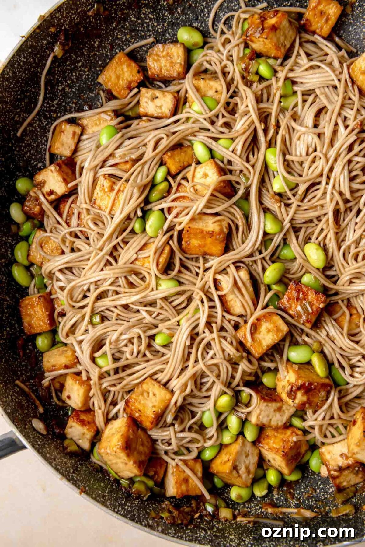 Sesame-Ginger Tofu Soba Noodles 9 Soba noodles and crispy tofu cubes cooking together in a skillet with bright green edamame beans mixed throughout.