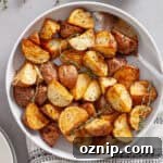 A serving bowl of crispy air fried red potatoes garnished with sprigs of fresh thyme.