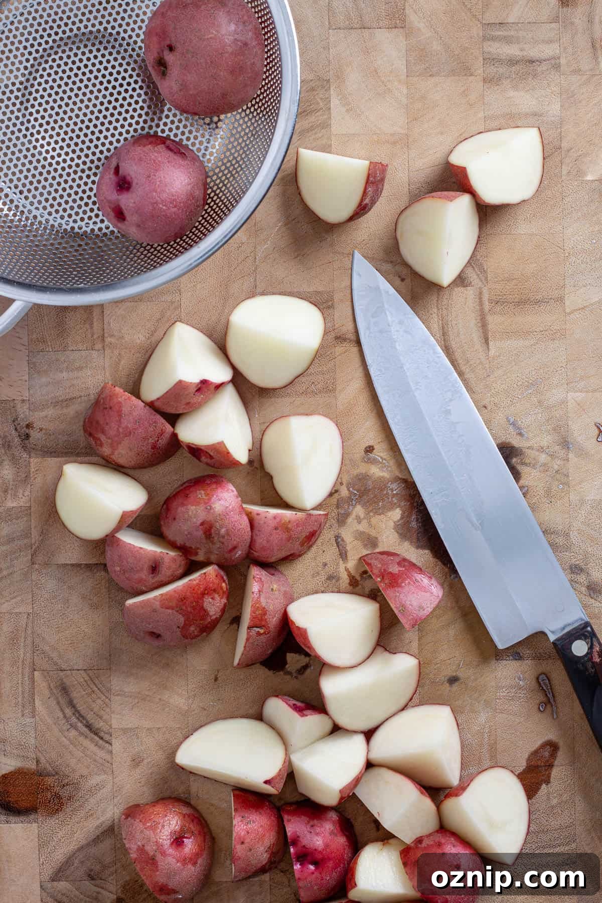 Red potatoes on a butcherblock cutting board getting chopped.