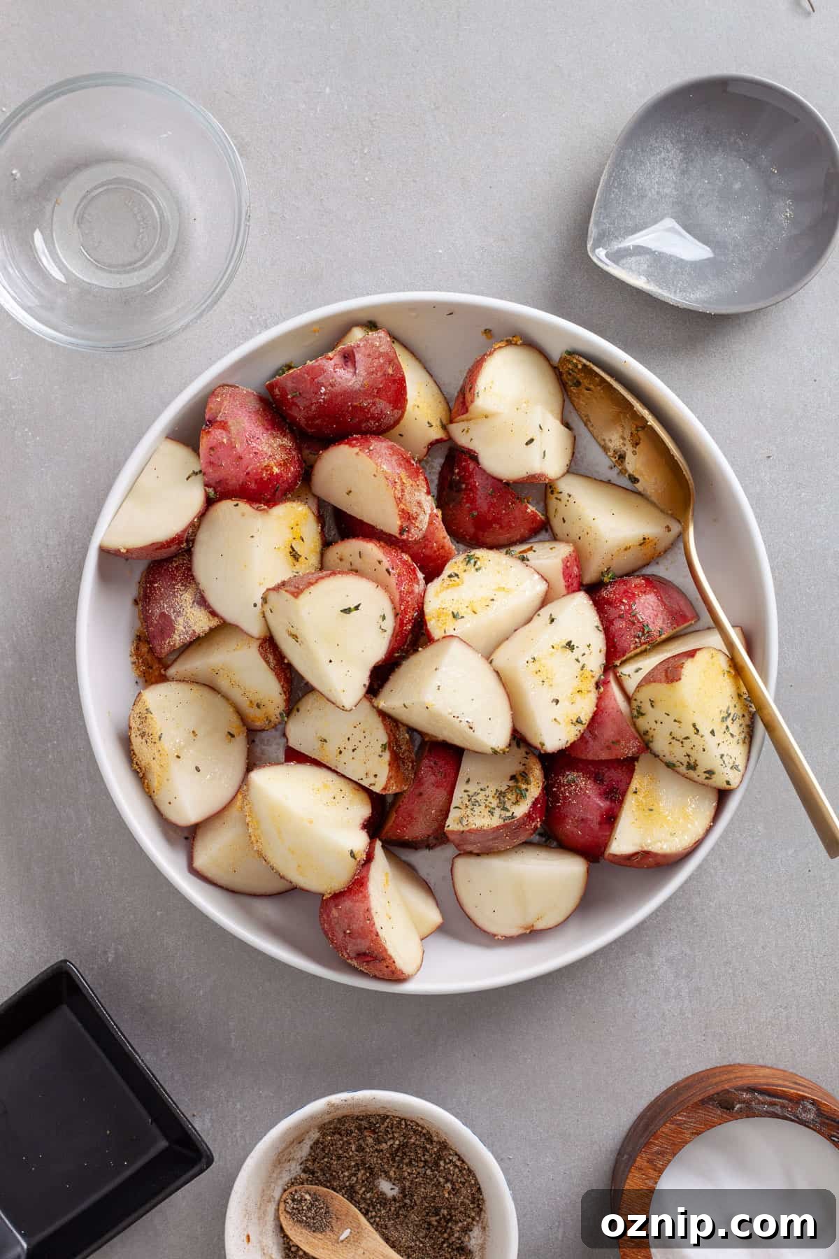 A bowl of chopped red potatoes seasoned with garlic powder, oil and fresh thyme.