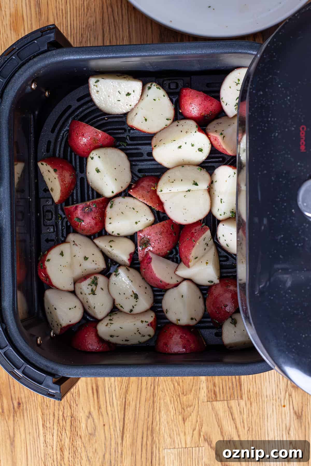 A basket of an air fryer filled with chopped seasoned red potatoes.