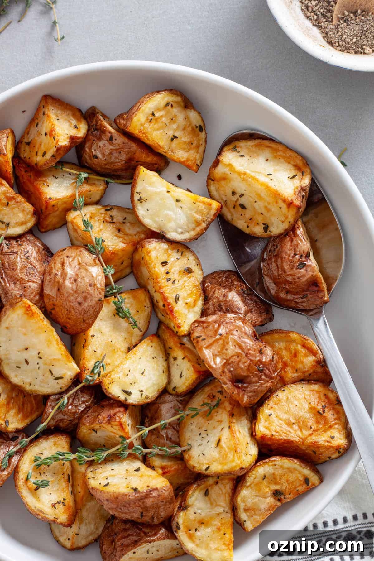A close up of a bowl of crispy air frier red potatoes garnished with fresh thyme.