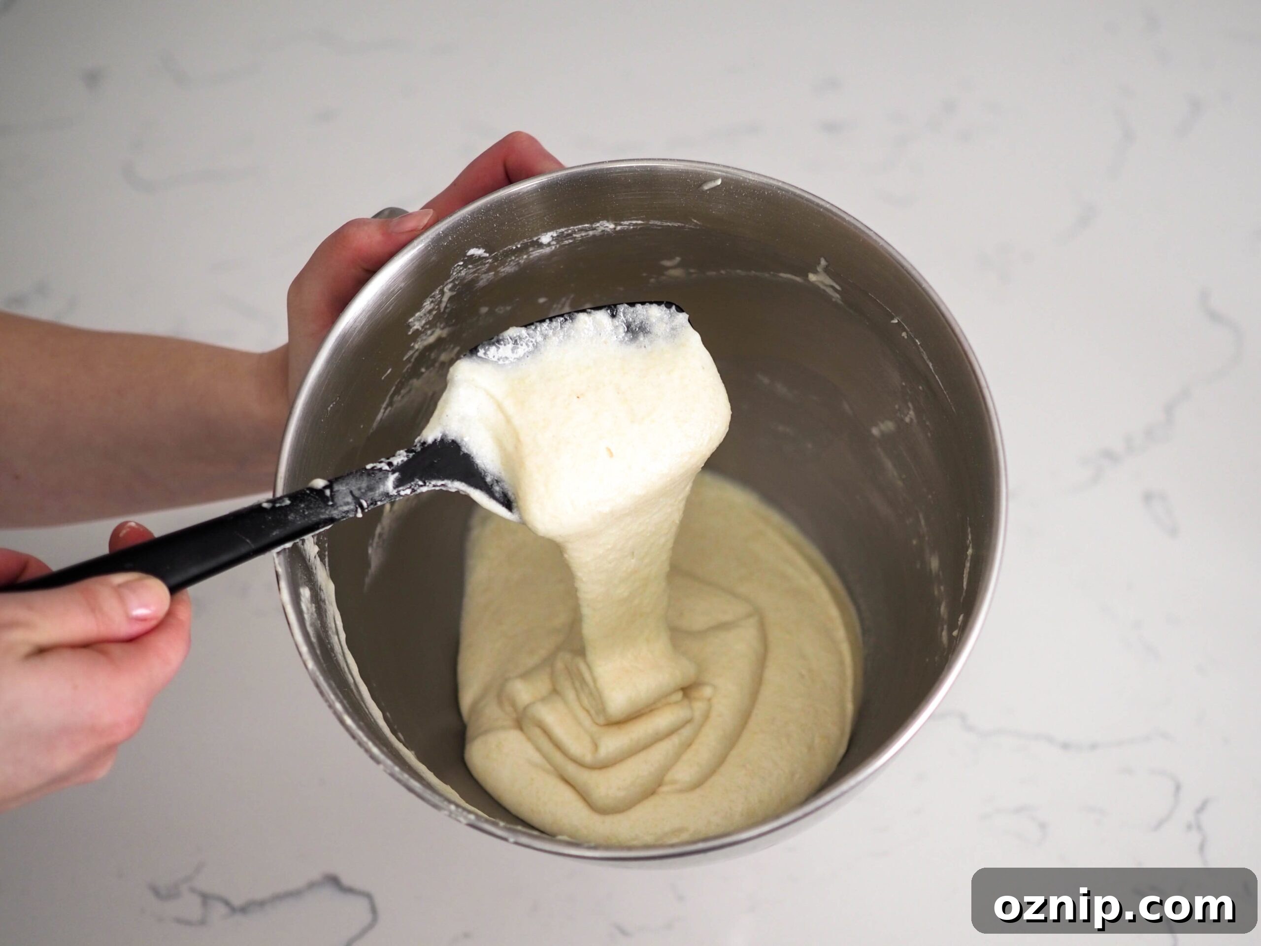 The macaron batter flows off the spatula in one long ribbon that stacks on top of itself in the bowl.