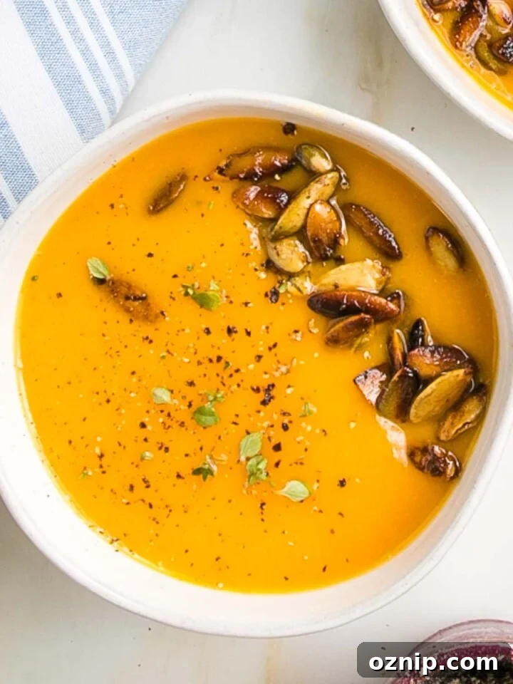 Bright orange creamy soup in a bowl with toasted pepitas, cracked pepper and fresh herbs.
