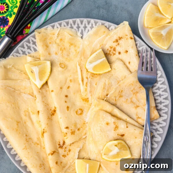 Overhead view of thin English pancakes on a plate with lemon and sugar