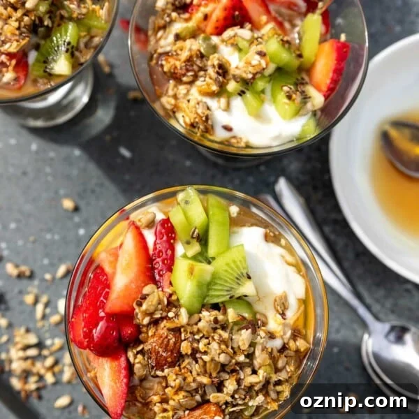 Overhead view of 3 Greek yogurt parfaits topped with honey, granola and chopped fresh strawberries and kiwi fruit
