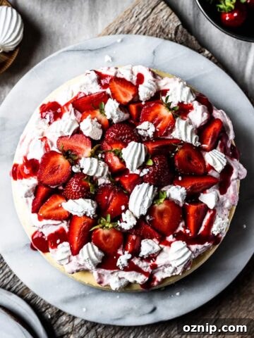 A top view of a vanilla cheesecake topped with whipped cream, strawberry coulis, and fresh strawberries.