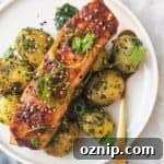 Miso glazed salmon on top of herby potatoes on a white plate, with sesame seeds, coriander and spring onion on top.