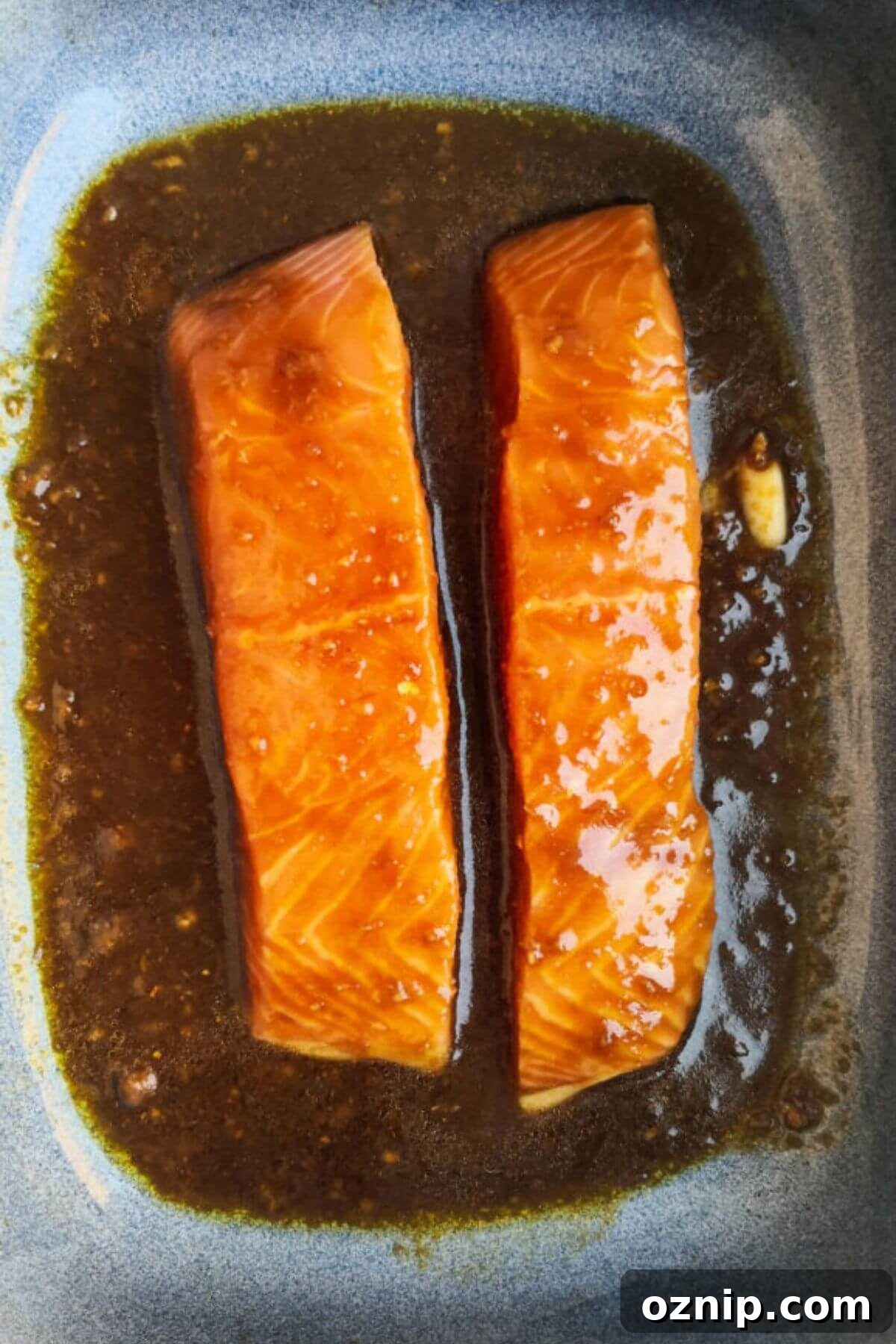 2 salmon fillets in a blue oven dish with miso marinade over the top.