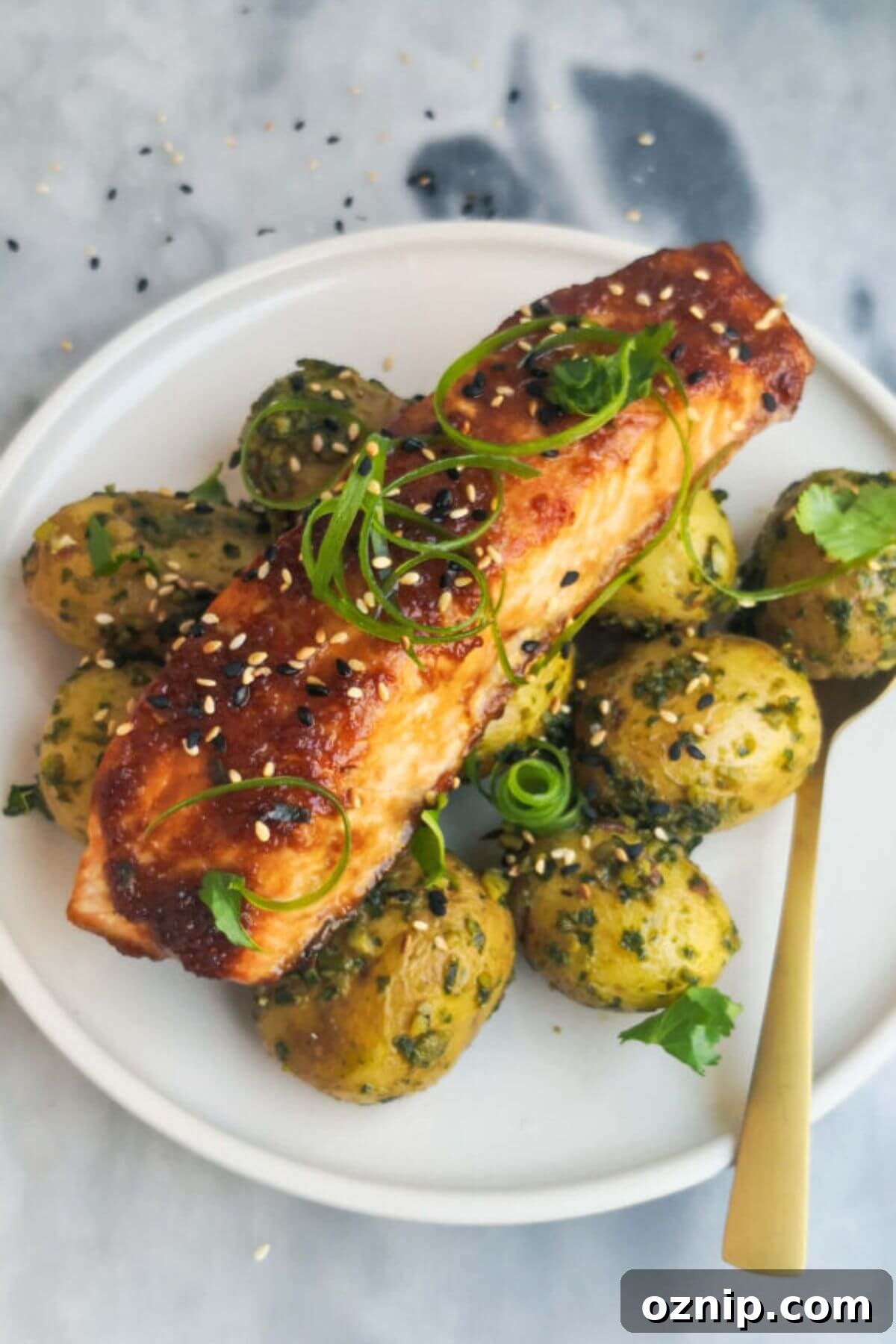 Piece of miso grilled salmon on a bed of herby potatoes on a small white plate.