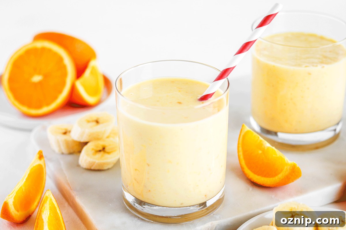 A glass of orange smoothie with a red striped straw with orange slices and banana slices around it.
