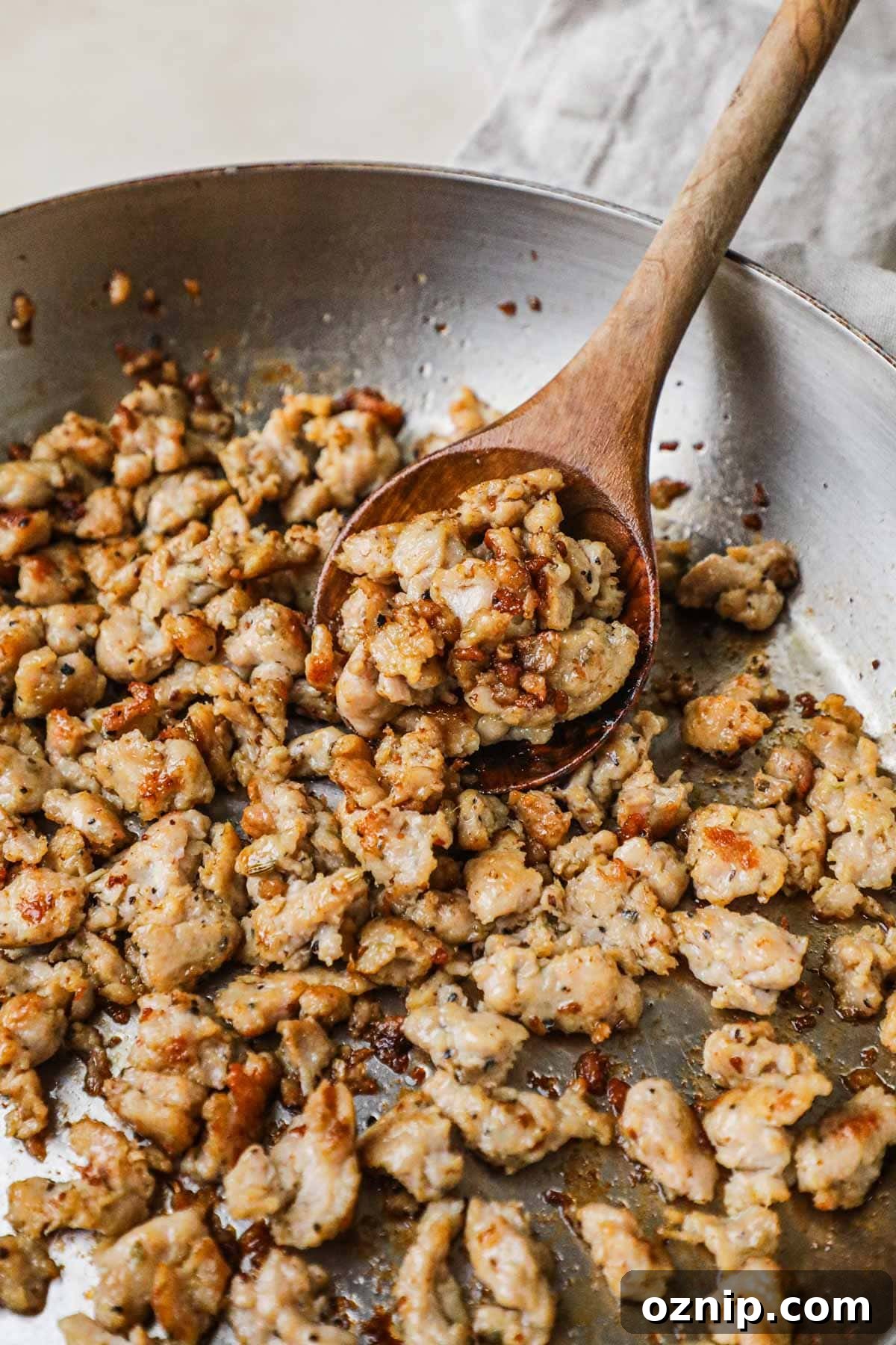 Caramelized and browned ground Italian sausage in a pan with a wooden spoon holding a scoop.