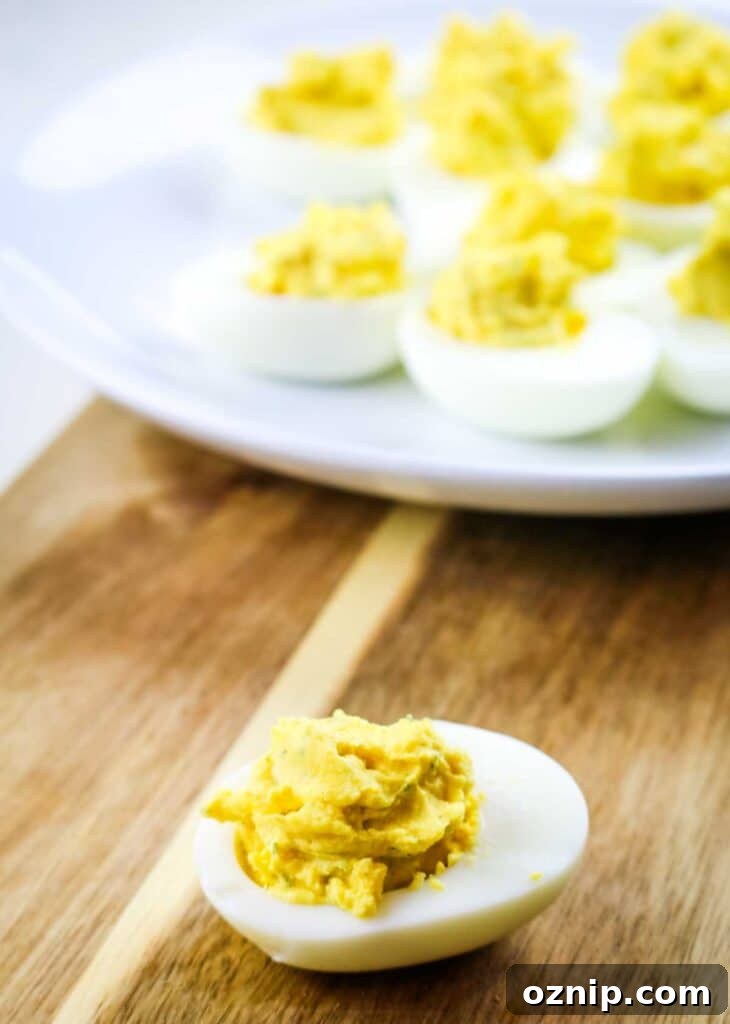 Classic Deviled Eggs Recipe for Parties 4 Deviled egg on a wooden cutting board with platter in the background.