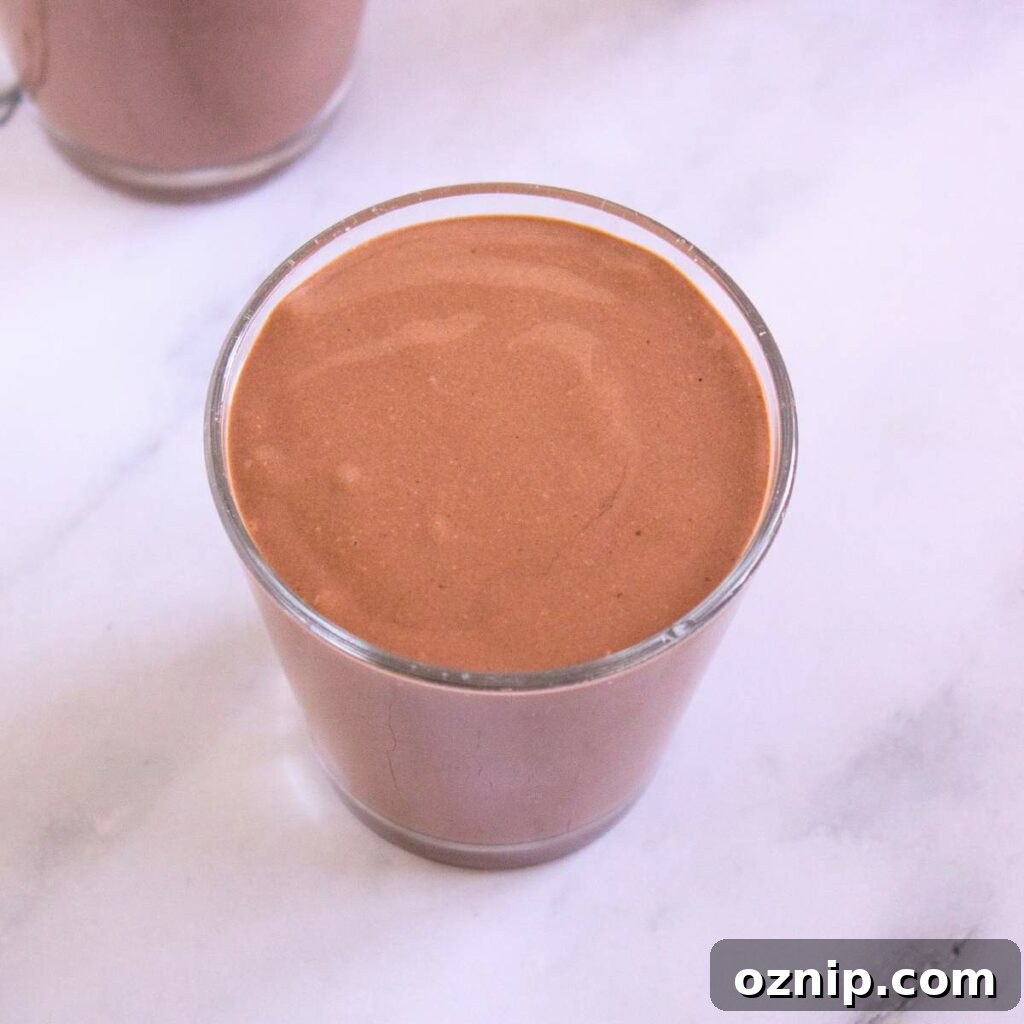 Low Carb Sugar Free Protein Pudding Recipe 13 A glass filled with chocolate protein pudding sits on a white marble surface.