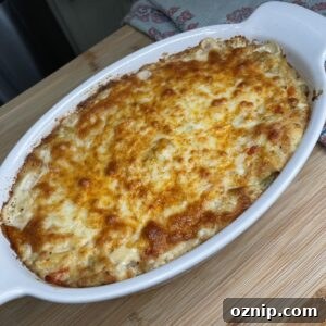 Creamy Crab and Artichoke Dip Recipe for Parties 4 A baked casserole dish filled with golden-brown, cheesy dip sits on a wooden surface next to a colorful, folded towel.