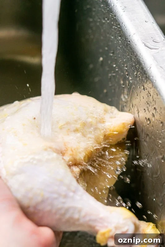 Rinsing a whole chicken in a sink, water running.