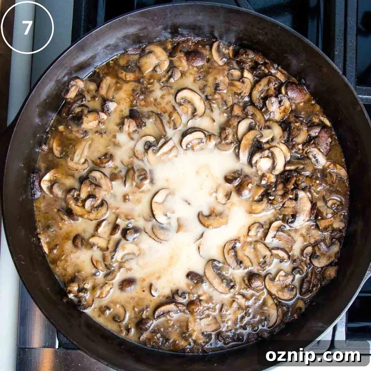 Sliced mushrooms cooked in brown sauce with a splash of white liquid in the center.
