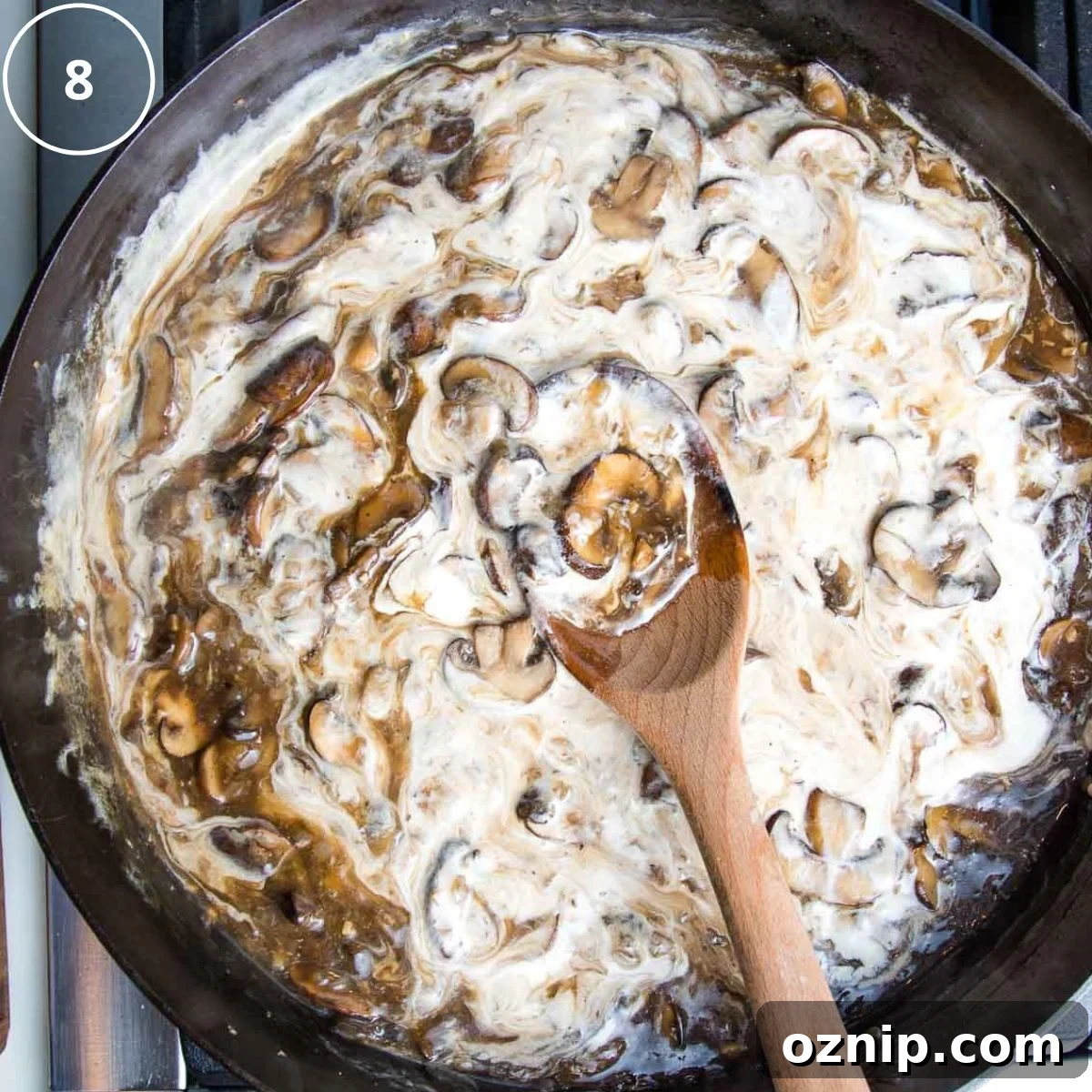 Sour cream being stirred into mushrooms in brown sauce.