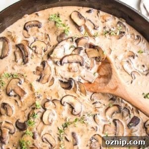 Close up of cast iron skillet filled with creamy vegan sauce, loaded with sliced mushroom, fresh thyme and a wooden spoon stirring it.