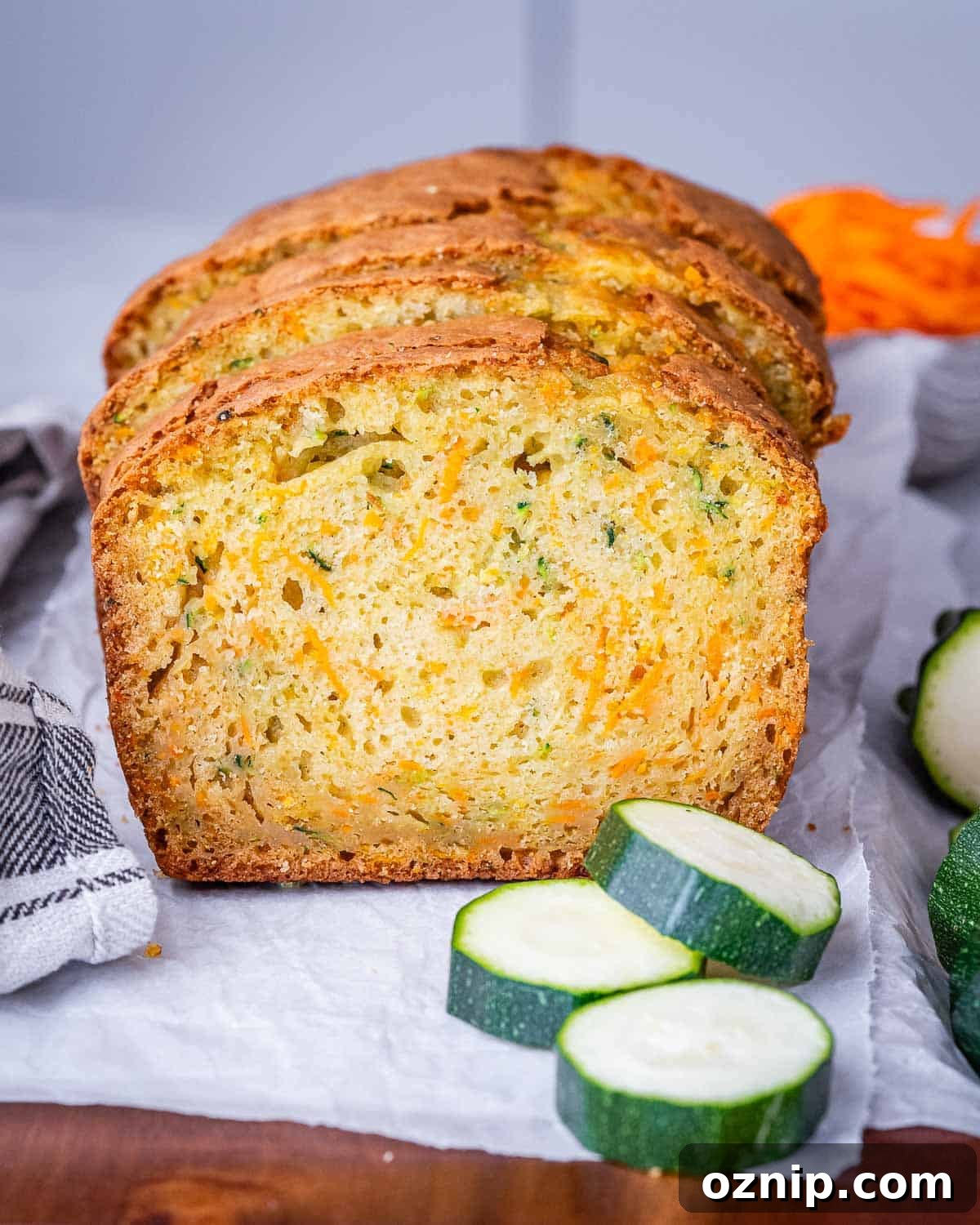 Close-up of a full loaf of zucchini carrot bread on a light gray surface with fresh zucchini slices.