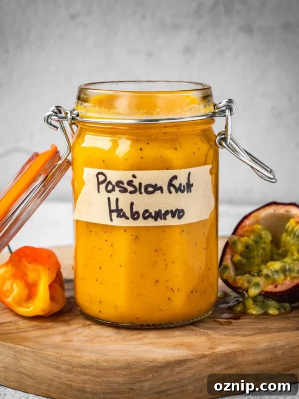 Passion fruit habanero in a jar with a fresh habanero pepper and an opened passion fruit on a board.