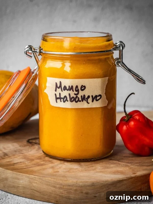 A jar of mango habanero hot sauce on a board with a mango and chile peppers.