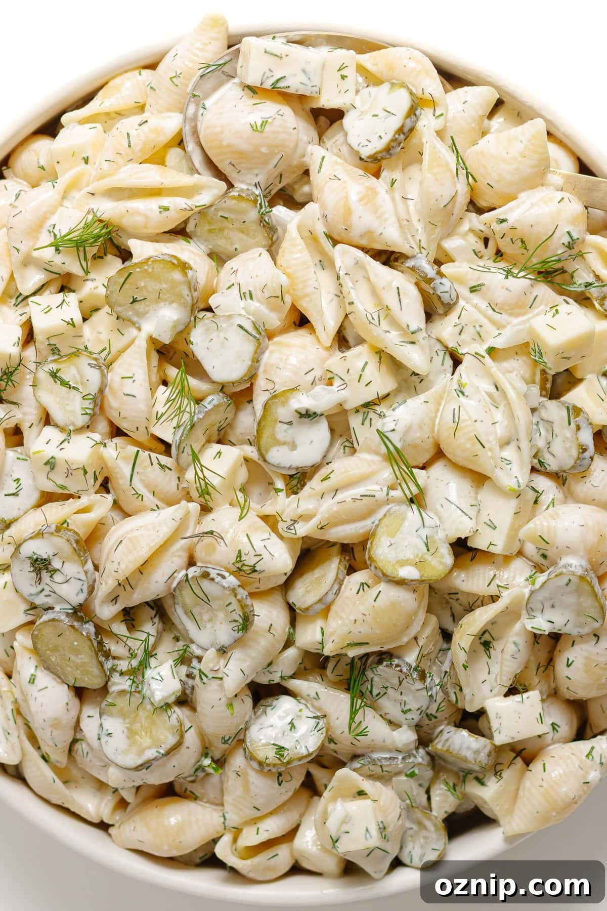 Dill pickle pasta salad in a white serving bowl with gold serving spoon.