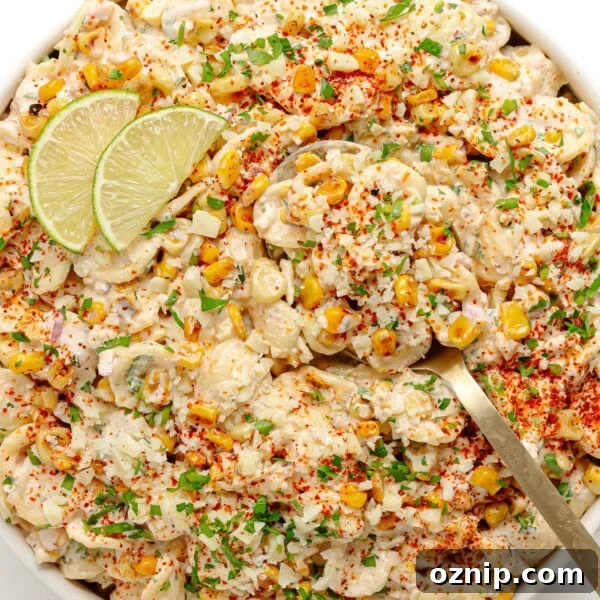 Elote pasta salad in a white serving bowl garnished with lime slices.