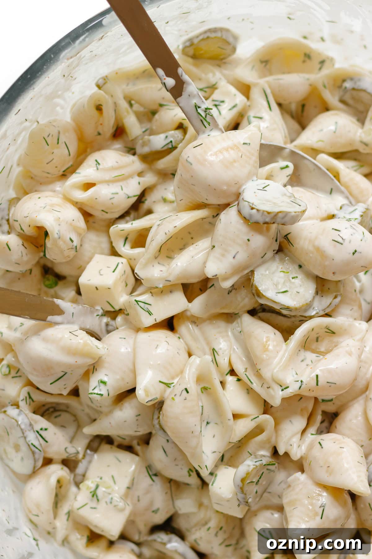 Dill pickle pasta salad being tossed together in a glass bowl.