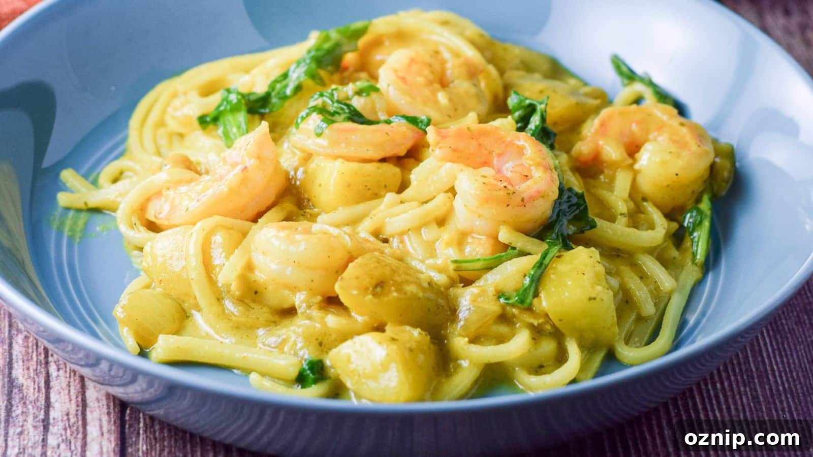 A blue deep bowl filled with noodles, shrimp and vegetables