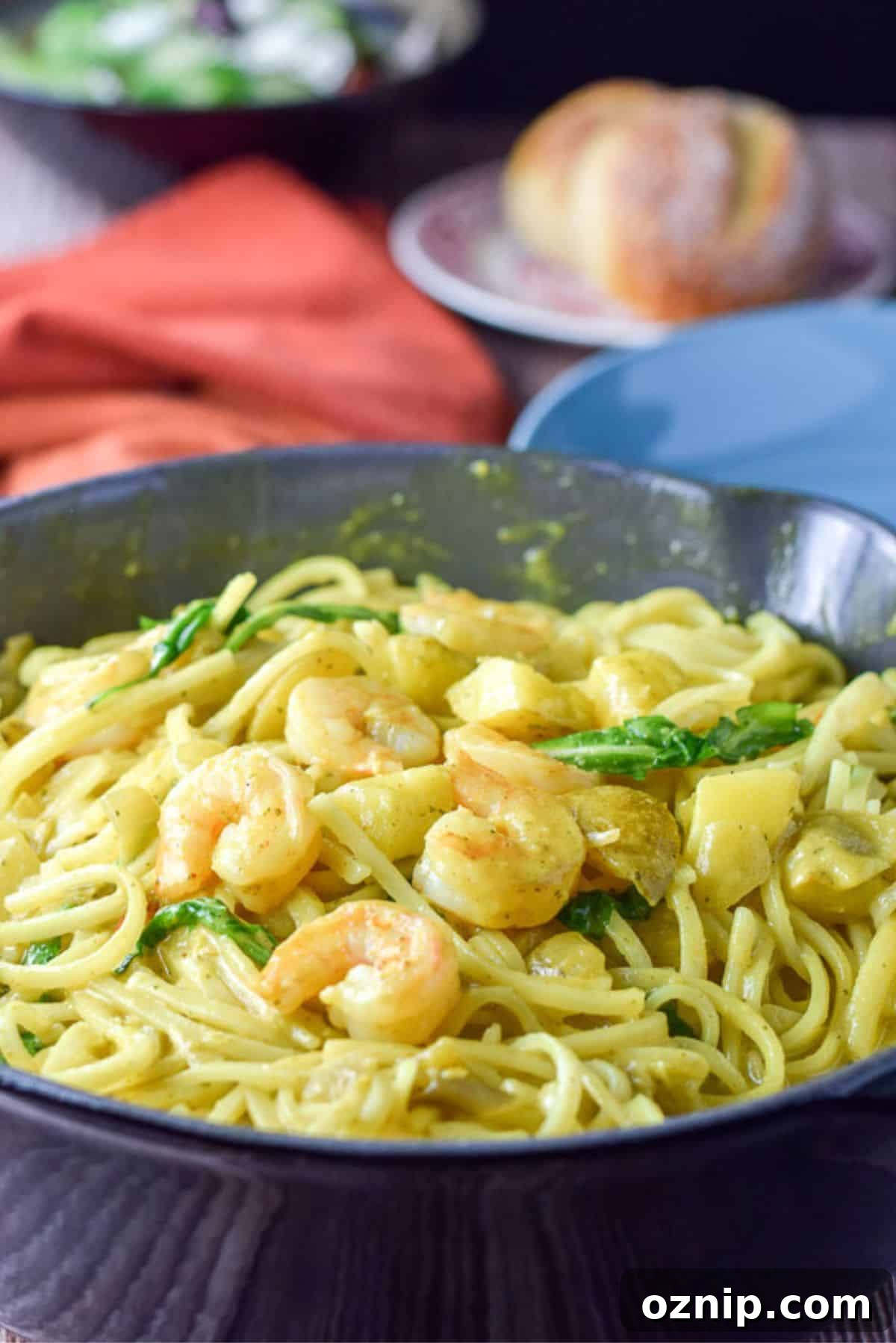 The shrimp on curry noodles in a big pan with a roll, plate and salad in the background