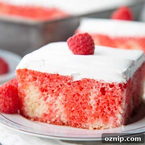 Red Jell-O poke cake topped with whipped cream and a raspberry.